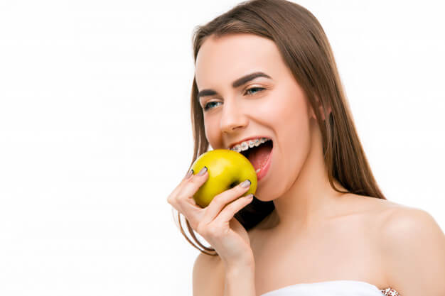 ortodontia paciente com aparelho odontologico comendo fruta