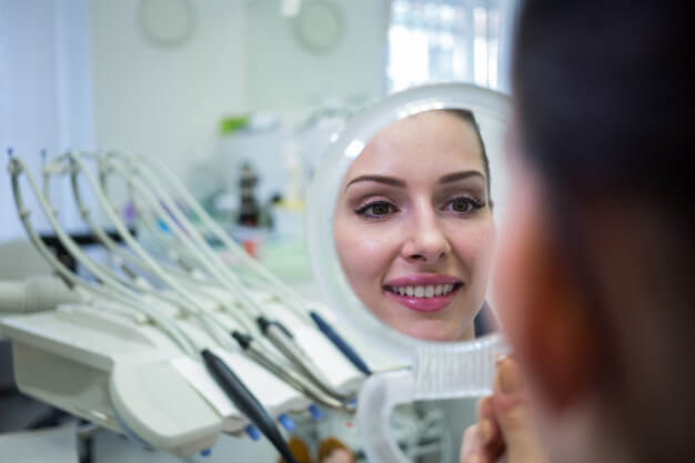 limpeza dentária mulher se olhando no espelho do dentista